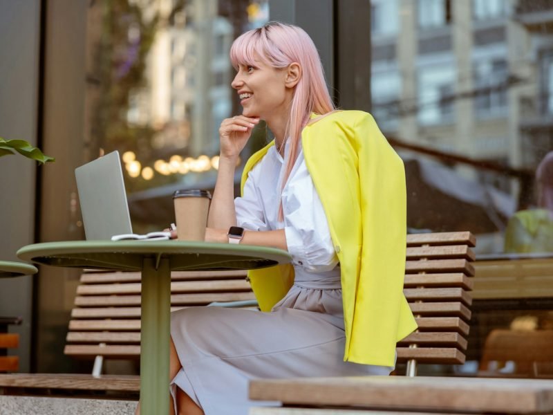 Joyful woman sitting at the table with laptop on the street