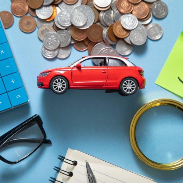 Red toy car, calculator and coins on the blue background.